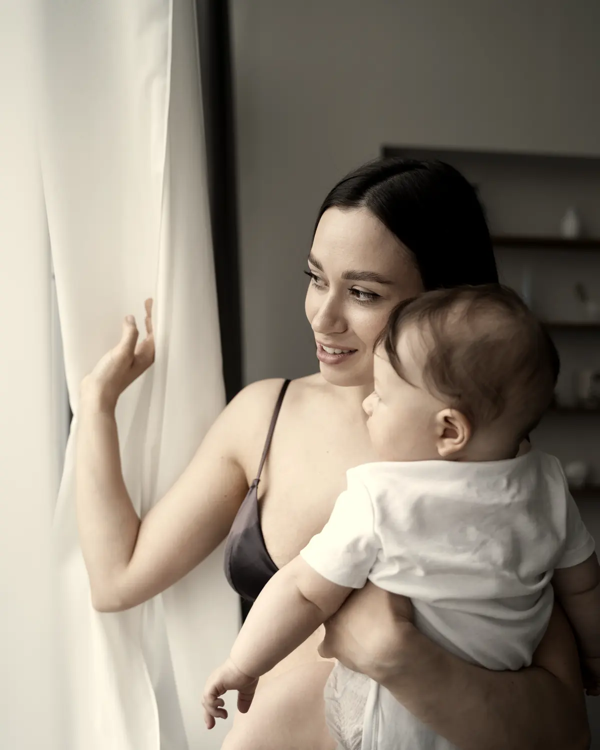 Mãe no colo com o bebê, junto à janela